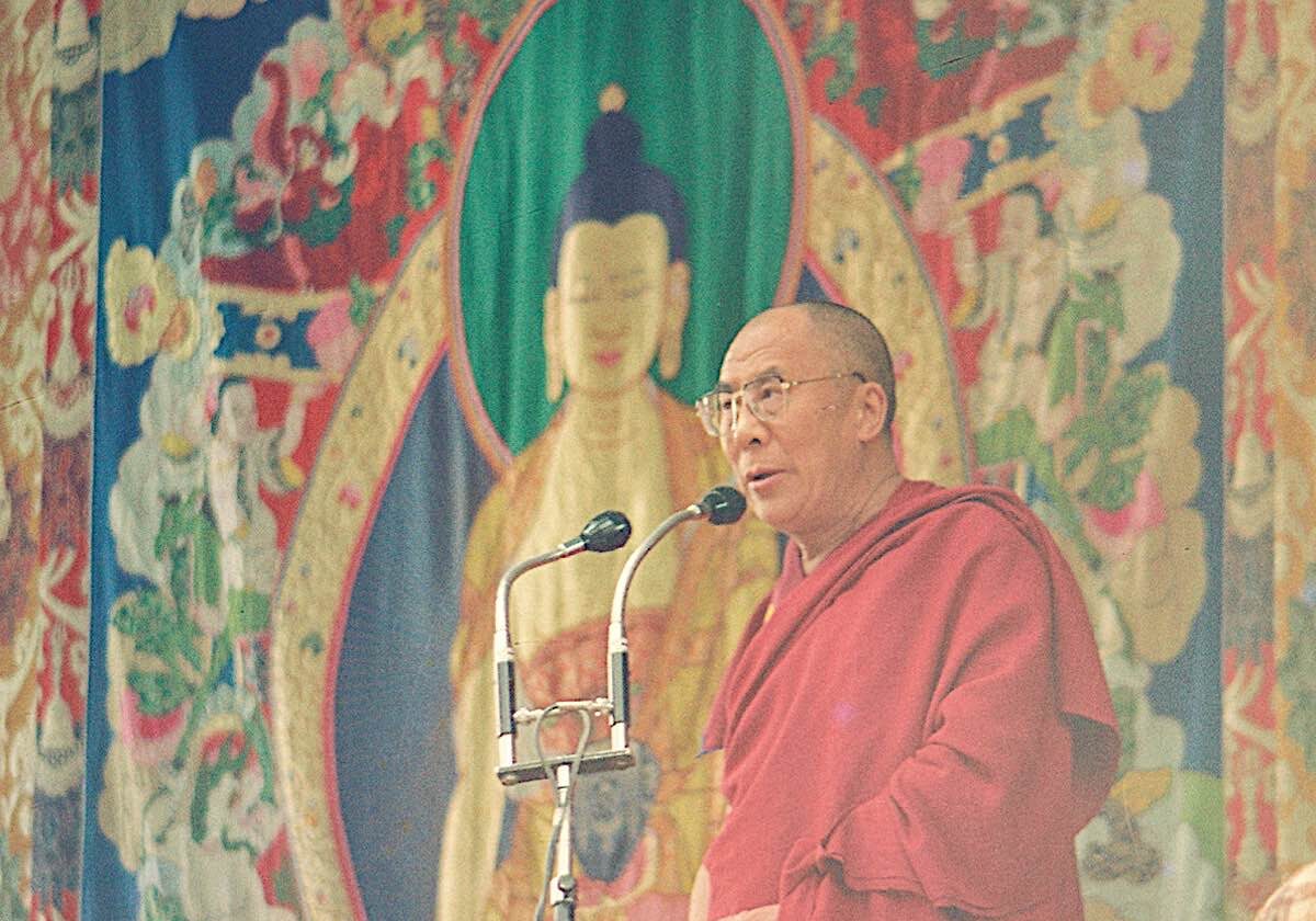 Buddha-Weekly-Dalai Lama speaking publicaly in front of one of the silk appliqué thangkas-Buddhism The Dalai Lama at a public speaking engagment stands in front of one of the appliqué thangkas of Shakyamuni Buddha.